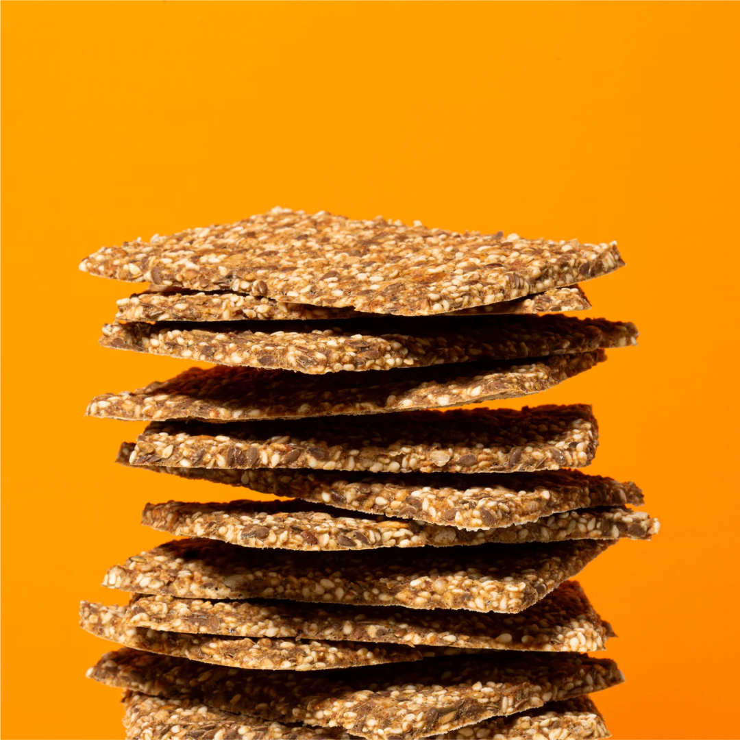 Stack of thin seeded crispbread crackers balanced against a bright orange background.